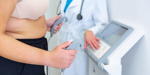 A health practitioner assists obese young woman with a body composition test using advanced equipment.